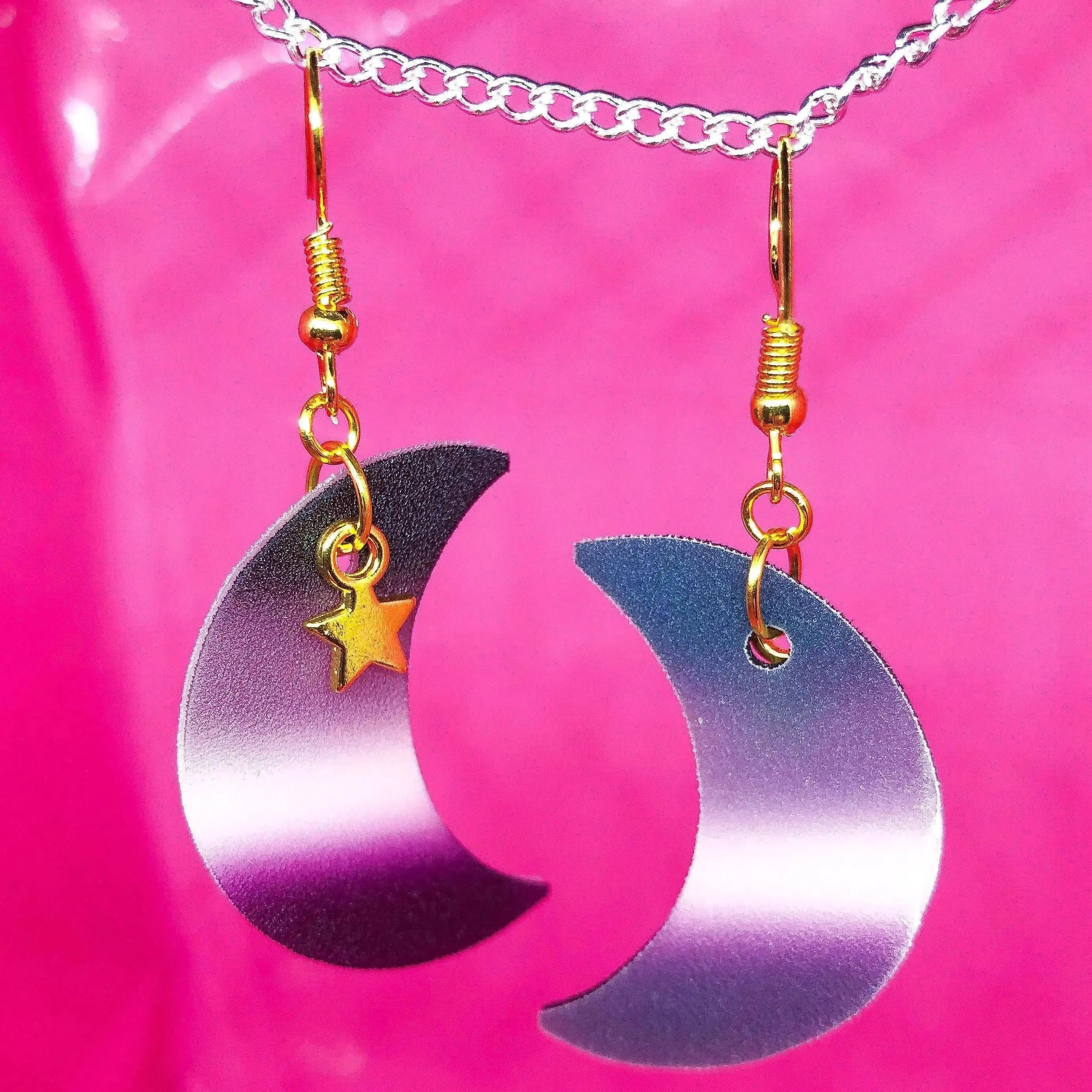 Shrinky dink earrings in the shape of a crescent moon. The colour of the charm is the asexual pride flag with a small gold star charm hanging at the top.