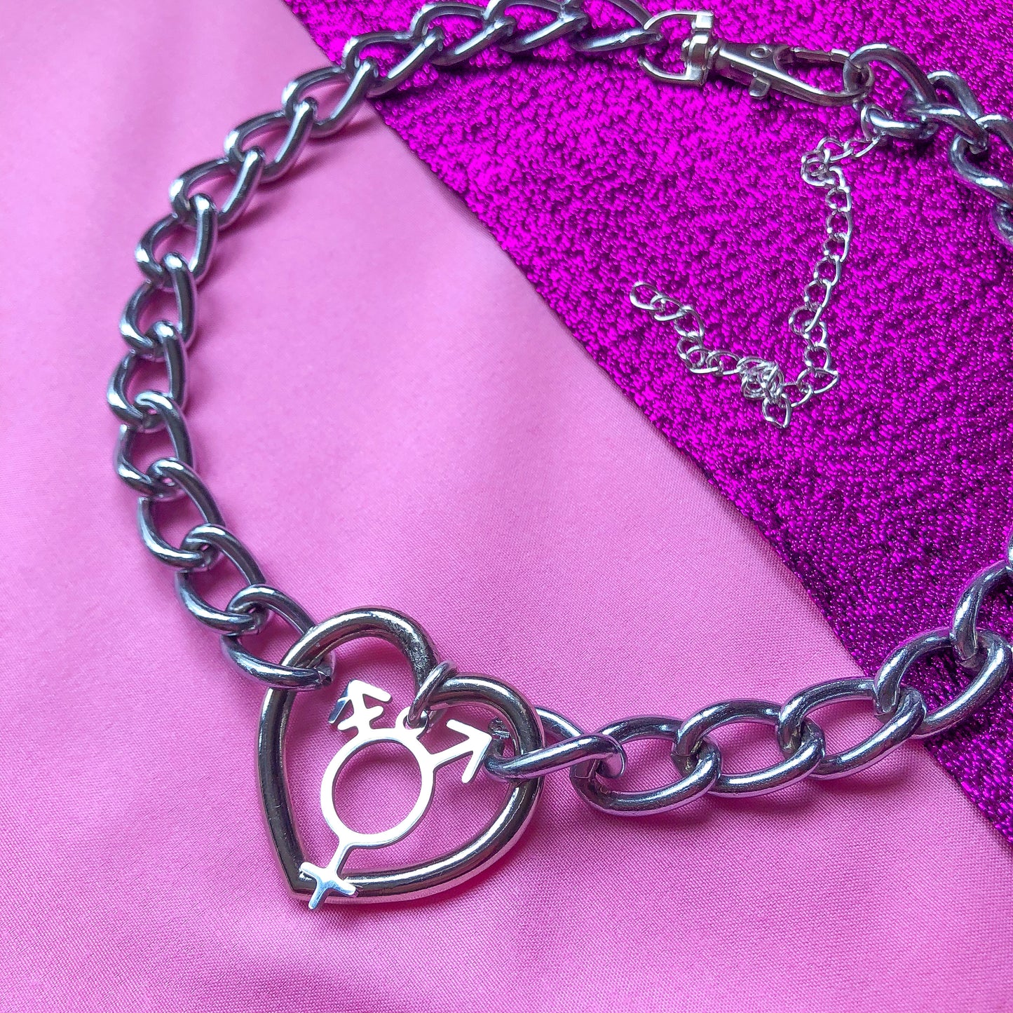 Chunky chain necklace with a love heart O ring in the middle, with a transgender symbol charm attached.